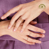 Close-up of hands wearing gold rings on a purple fabric background with Fairmined logo.