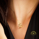 Gold necklace with a geometric dodecahedron pendant worn by a woman, against a black background.