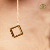 Gold hexahedron dangle and drop earring close-up on a blurred background.