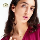 Woman wearing gold pyramidal earrings and necklace with Fairmined logo.