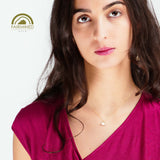 Woman wearing a pink top and a gold necklace with a tetrahedron pendant on a white background