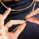Close-up of hands holding a silver necklace clasp against a dark fabric background
