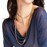 Woman wearing a blue top with layered silver necklaces on a white background