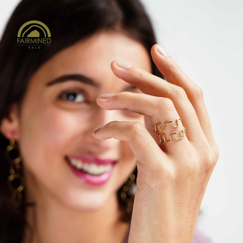 Woman wearing two gold rings with a blurred background and Fairmined logo.