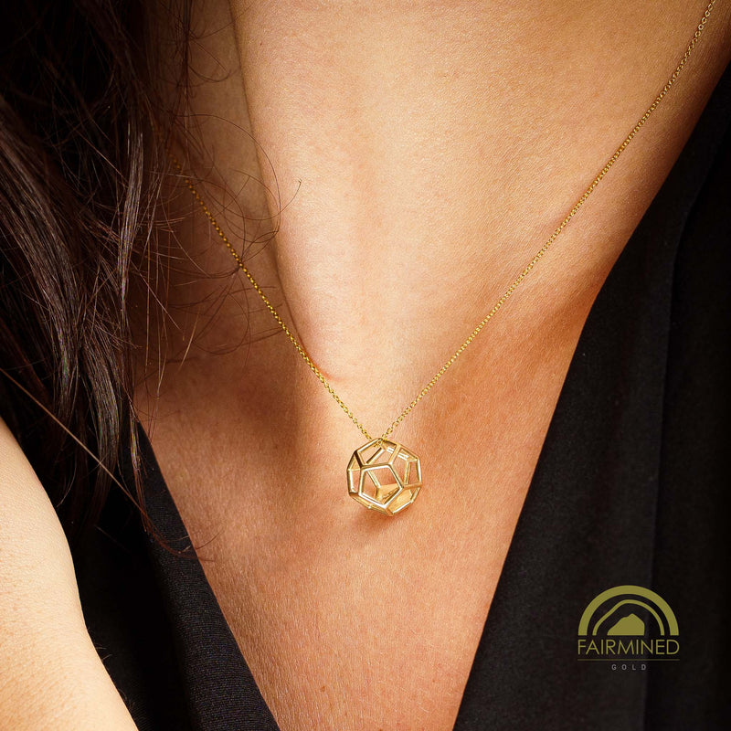 Gold necklace with a geometric dodecahedron pendant worn by a woman, against a black background.
