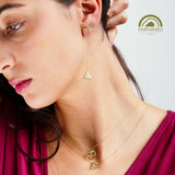 Close-up of a woman wearing gold pyramidal earrings and necklaces against a neutral background