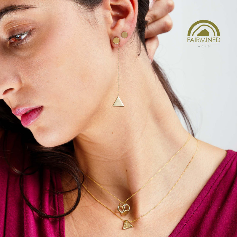 Close-up of a woman wearing gold pyramidal earrings and necklaces against a neutral background