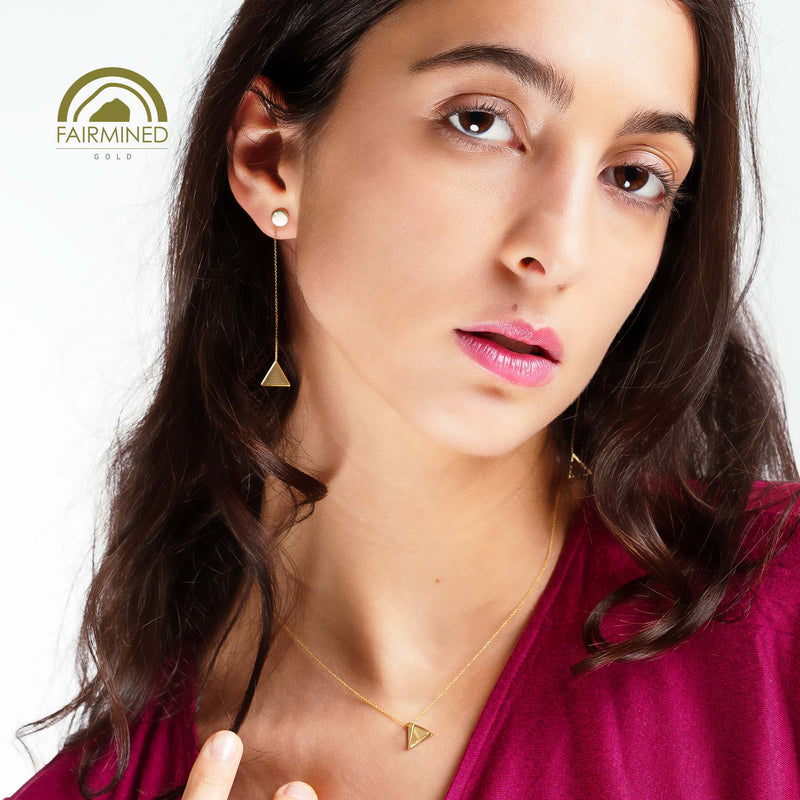 Woman wearing gold pyramidal earrings and necklace with Fairmined logo.
