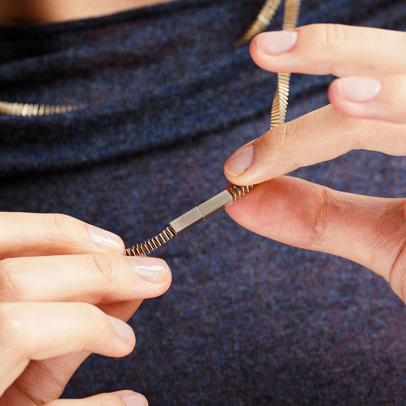 Close-up of hands holding a small metallic magnetic clasp object against a textured blue background